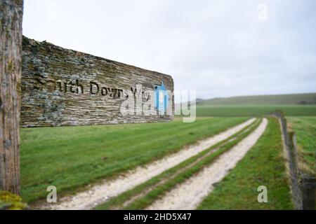 South Downs Way Fingerpost zeigt auf den Hintergrund entlang eines Weges, der in die Ferne führt, neben einer Graswiese unter einem bewölkten, bewölkten Himmel. Stockfoto