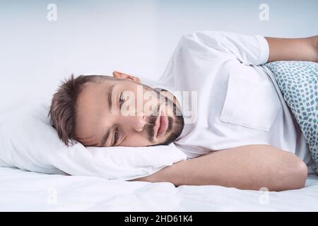 Gestresster und deprimierter Mann, der im Bett liegt. Mann fühlt sich schlecht, verzweifelt und hilflos Stockfoto