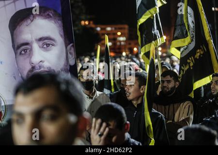 Gaza-Stadt, Palästina. 03rd Januar 2022. Demonstranten des Palästinensischen Islamischen Jihad halten Flaggen und Bilder von Hisham Abu Hawasch, 40, der seit mehr als 140 Tagen in einem Hungerstreik ist, nachdem er von Israel verhaftet und in Verwaltungshaft genommen wurde. Kredit: SOPA Images Limited/Alamy Live Nachrichten Stockfoto