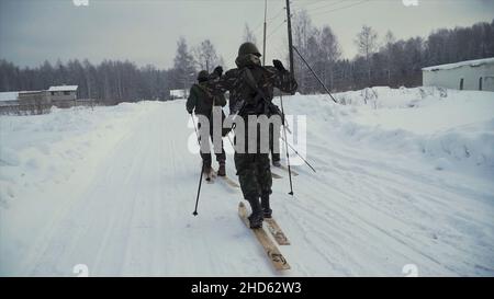 Eine Gruppe von Soldaten laufen mit Waffen auf Skiern im Wald. Clip. Soldaten mit AK-47-Gewehren und Granatwerfer laufen auf s durch den Winterwald Stockfoto