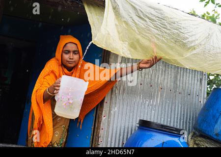 Mongla, Bangladesch. 12th September 2021. Eine Frau sammelt Regenwasser mithilfe einer Kunststofffolie unter dem Zinndach ist Regenwasser die Hauptquelle für Trinkwasser im Küstengebiet des Dorfes Jaymani.Bangladesch ist eines der Länder, die am stärksten von den Auswirkungen des Klimawandels betroffen sind. Die regelmäßigen und schweren Naturgefahren, die Bangladesch bereits unter tropischen Wirbelstürmen, Hochwasser, Flußerosion, Überschwemmungen, Erdrutschen und Dürren leidet, werden durch den Klimawandel immer intensiver und häufiger werden. (Foto von Sultan Mahmud Mukut/SOPA Image/Sipa USA) Quelle: SIPA USA/Alamy Live News Stockfoto