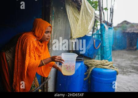 Mongla, Bangladesch. 12th September 2021. Eine Frau sammelt Regenwasser, indem sie eine Plastikfolie unter dem Blechdach verwendet, Regenwasser ist die Hauptquelle des Trinkwassers, da der Salzgehalt aufgrund der hohen Gezeiten während des Zyklons im Küstengebiet des Dorfes Jaymani zunimmt.Bangladesch ist eines der Länder, die am stärksten von den Auswirkungen des Klimawandels betroffen sind. Die regelmäßigen und schweren Naturgefahren, die Bangladesch bereits unter tropischen Wirbelstürmen, Hochwasser, Flußerosion, Überschwemmungen, Erdrutschen und Dürren leidet, werden durch den Klimawandel immer intensiver und häufiger werden. (Kredit Stockfoto