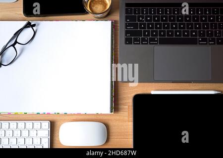 Nahaufnahme des Arbeitsplattes im Büro mit Holztisch und Laptop-Verlegung, Arbeitsplatz. Komfortabler Arbeitsplatz mit Laptop Espresso Smartphone Notizblock Papier Stift Brillen Maus darauf legen. Hochwertige Fotos Stockfoto