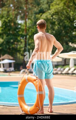 Ein Mann in blauen Shorts, der in der Nähe des Pools mit einem Schlauch in den Händen steht Stockfoto