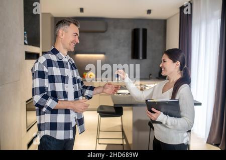 Glücklicher Mann, der Schlüssel von der immobilienmaklerin im Haus nimmt Stockfoto