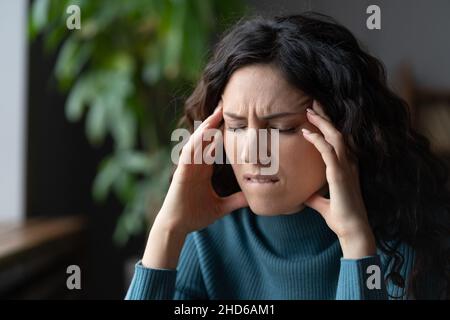 Unglücklich gestresste Frau, die an Kopfschmerzen am Arbeitsplatz leidet, ängstliche Frau, die Kopfschmerzen im Kopf hat Stockfoto