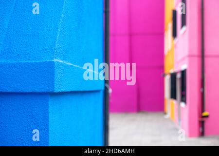 Nahaufnahme der Ecke einer leuchtend blauen Gipsfassade mit einer rauhen Oberfläche vor einem farbenfrohen rosa Bokeh-Hintergrund Stockfoto