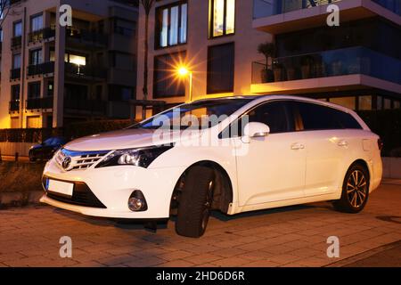 Weißer Toyota Avensis, aufgenommen im Dunkeln vor städtischem Hintergrund (Ludwigshafen, 16. Februar 2021) Stockfoto