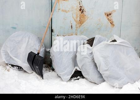 Vier Winterreifen in Zellophan gewickelt, die vor einer Metallgarage platziert wurden, Winterszene Stockfoto