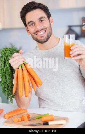 Schöner Mann, der in der Küche Karottensaft hält Stockfoto