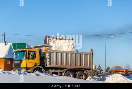 23. Dezember 2021. Region Kemerowo, Russland. Großer orangefarbener Traktor reinigt Schnee von der Straße und lädt ihn in den LKW. Reinigung und Reinigung der Straße Stockfoto