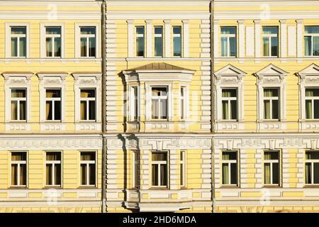 Gelbe Gebäudefassade mit klassischer Architektur und gerahmten Fenstern als Hintergrund. Fragment der alten Gebäudefassade. Stockfoto