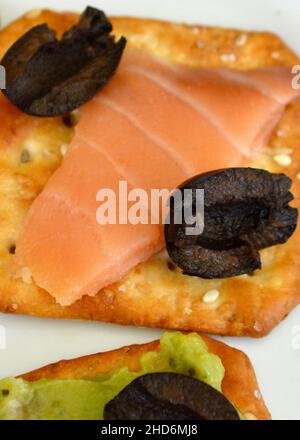 Aufgeschnittener Atlantischer Lachs auf einem Cracker-Keks mit schwarzen Oliven Stockfoto