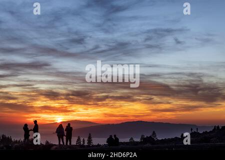 Teneriffa, Kanarische Inseln, Spanien. 3rd Januar 2022. Touristen beobachten den dramatischen Sonnenuntergang hinter den Inseln El Hierro und La Gomera aus einer Höhe von etwa 2000 Metern über dem Meeresspiegel auf der Seite des Vulkans Teide auf Teneriffa auf den Kanarischen Inseln. Stockfoto