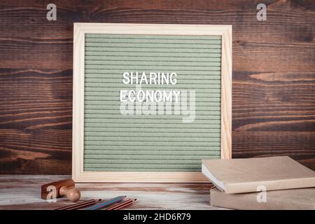 GEMEINSAME NUTZUNG DER WIRTSCHAFT. Englischer Text auf einem Brief Board. Schreibwaren auf einem Holztisch. Stockfoto