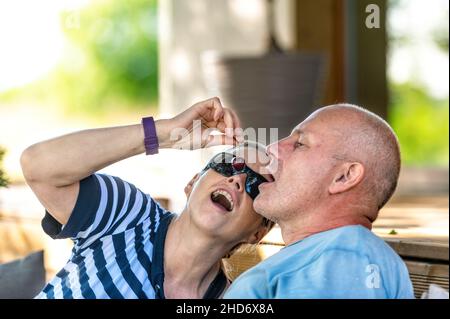 Glückliches Ehepaar, das sich gegenseitig mit Kirschen fütterte, sich im Freien erholte und flirterte Stockfoto
