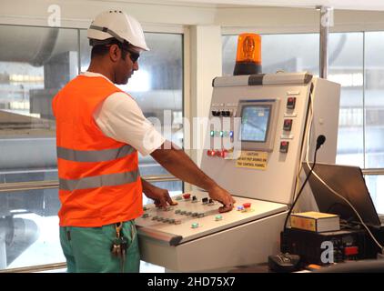 Ein Ingenieur, der eine hohe Sichtweite und Schutzhelm trägt, betreibt eine Schalttafel in einer Aluminiumschmelzanlage. Stockfoto