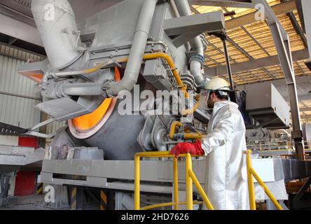 Aluminium-Recycling. Ein Mann in schützender, hitzebeständiger Kleidung überwacht einen Aluminium-Rückgewinnungsofen, der in einer großen Schmelzanlage in Betrieb ist. Stockfoto