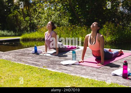 Junge Frauen in Sportbekleidung üben Yoga auf Übungsmatten im öffentlichen Park Stockfoto