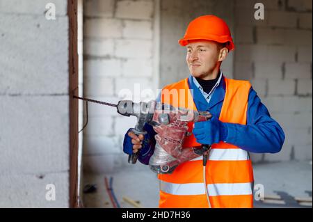 Builder in Hardhat arbeiten mit Bohrer in Innenräumen Stockfoto