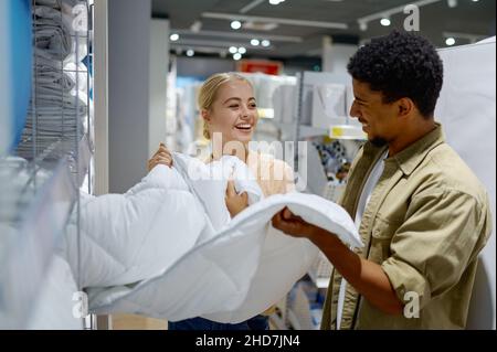 Glückliches multirassisches Paar, das Decke im Geschäft kauft Stockfoto
