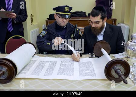 Bei einer Zeremonie, bei der das Schreiben einer neuen Tora gefeiert wird, nimmt ein jüdischer Polizist am Ritual Teil, einen Brief zu feigen. In Bayside, Queens, New York. Stockfoto