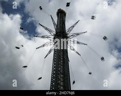 Unterhaltungskonzept - Hochdrehendes Schaukelkarussell von unten im berühmten Prater in Wien, Österreich. Blauer Himmel und Wolken im Hintergrund. Stockfoto