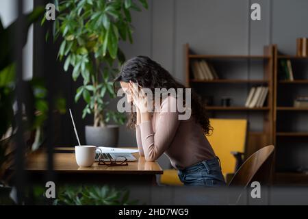 Junge frustrierte weibliche Mitarbeiterin am Arbeitsplatz vor dem Laptop, die bei der Arbeit oder dem Projekt feststeckt Stockfoto