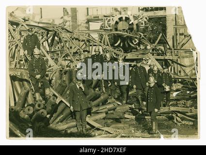 Pressefoto eines verheerenden Feuers in einer Linoleum-Fabrik in Muswell Hill, London, WC1, Anfang des 20. Jahrhunderts. Die Feuerwehrleute tragen typische „Merryweather“ Messinghelme, die in der viktorianischen Ära entworfen wurden, und doppelreihige Tuniken, es gibt andere Feuerwehrleute, die Mützen tragen, der Mann vorne links scheint Notizen zu machen, vielleicht ein Inspektor, der den Schaden untersucht. Um 1929. Stockfoto