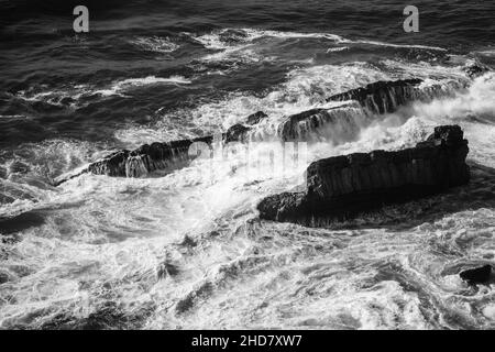 Wellen aus dem Meer mit seiner Brandung nähern sich dem Strand, von oben gesehen, die in den Felsen krachen Stockfoto