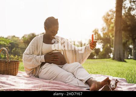 Junge afrikanische Frau, die Spaß hat, Videoanruf im Stadtpark zu machen - Fokus auf Gesicht Stockfoto