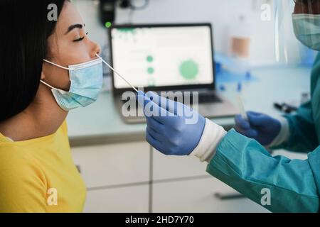 Arzt, der jungen Frauen in der medizinischen Klinik einen Nasentest für eine Coronavirus-Infektion macht - Fokus auf die Hand mit dem Tupfer Stockfoto