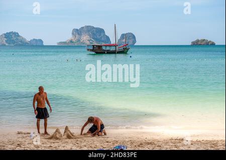 Zwei junge Männer bauen am Prah Nang Beach auf der Halbinsel Railay Beach, einem der schönsten Strände Thailands, eine Sandburg. Stockfoto