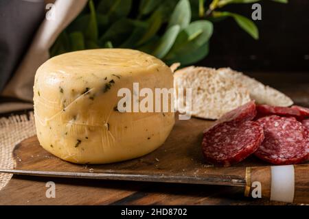 Ein kleines gewürztes Käsestück auf einem Brett mit Brot und Salami. Normale Ansicht. Stockfoto