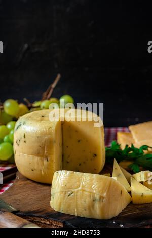 Eine normale Ansicht eines köstlichen kleinen Stückes gewürztem Käse auf einem Brett neben einem in Scheiben geschnittenen Provolon-Käse. Konzept der natürlichen, biologischen und gesunden Ernährung. Cop Stockfoto