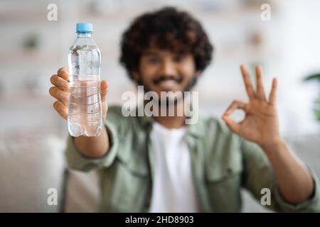 Glücklicher junger inder, der eine Flasche mit Wasser zeigt Stockfoto