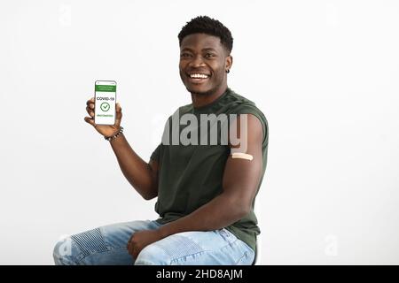 Heiter geimpfter schwarzer Kerl zeigt Smartphone mit Zertifikat Stockfoto