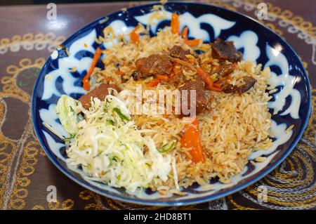 Tadschikischer Pilaf mit Karotten und Fleisch, Kohlsalat auf einem Teller mit Muster Stockfoto