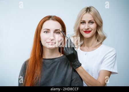 Master Kosmetikerin macht Markup von Augenbrauen Tätowierung, Frauen vor der Anwendung von Permanent Make-up, dauerhafte Augen Make-up und Augenbrauen Korrektur Verfahren. Happy Client Mädchen ist sehr zufrieden Stockfoto