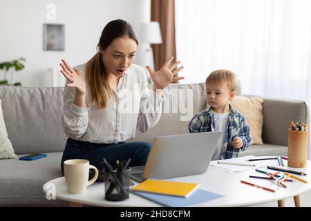 Nervöse junge Mutter von Kleinkindern, die von zu Hause aus arbeiten, Probleme mit dem Laptop zu Hause leiden und emotional auf Nachrichten reagieren Stockfoto