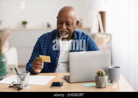 Senior African Male Shopping Online-Zahlung Mit Laptop Indoor Stockfoto