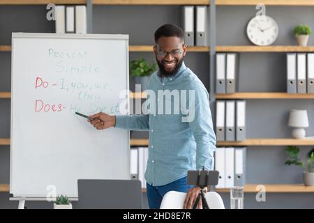 Frod freundlich Millennial afroamerikanischen männlichen Blogger Lehrer weist auf englische Regeln auf Tafel Stockfoto