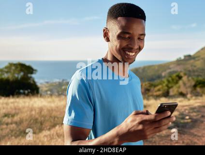 Schwarzer junger Erwachsener, lächelnd, während er sein Handy benutzte, um einen Bergspaziergang zu beginnen. Schöne Aktivitäten im Freien. Stockfoto