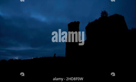 Mystische Silhouette eines Tempels oder einer Burg gegen den bewölkten Himmel und Raben, die nachts am Himmel fliegen. Video. Das große alte Steinschloss auf dem Rock du Stockfoto