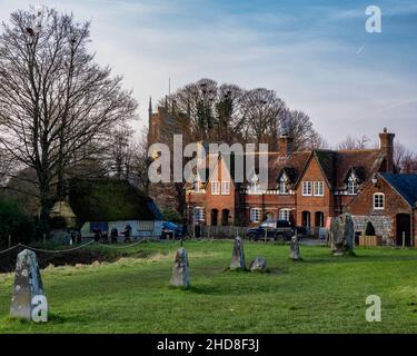 Winteransicht der St James Kirche und der Ziegelhütten in Avebury in Wiltshire UK mit Markierungsmasten von fehlenden stehenden Steinen von Hengé Perimeter Stockfoto