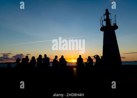 Silhouette einer mittleren Gruppe von Menschen, die den Sonnenuntergang vom Leuchtturm Ponta do Humatia in Salvador, Bahia, Brasilien, genießen. Stockfoto