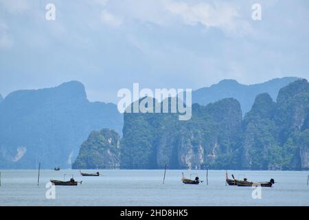 Fischerboote liegen vor der dramatischen Kulisse der hohen Klippe Karstinseln in Phang Nga N.P., Ko Yao Noi, Thailand Stockfoto