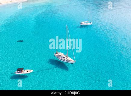 Boote, die auf einem ruhigen, türkisfarbenen Meeresgrund vor Anker liegen, Blick auf die Drohne aus der Luft. Griechenland, die Insel Elafonisos, Sandstrand mit Doppelstrand, sonniger Sommertag Stockfoto