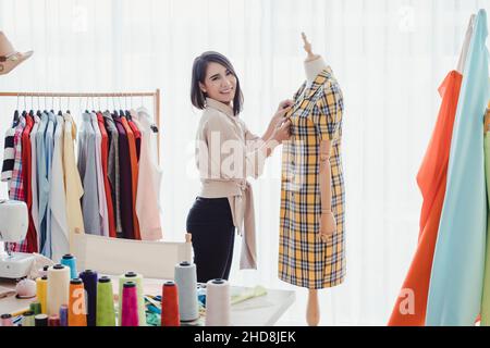 Schöne asiatische Frau Designer trägt Kleidung für ein Holzmodell nach dem Schneiden der Kleidung, um die Details der Kleidung für die custome geschnitten zu überprüfen Stockfoto