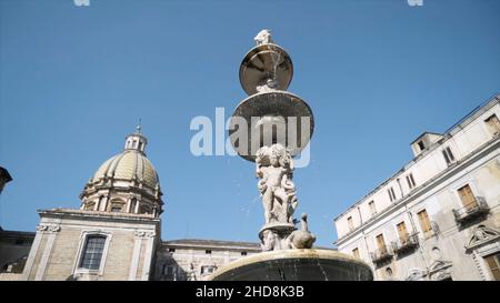 Blick von unten auf einen schönen Brunnen vor der Kathedrale. Monumentaler Brunnen mit einer Skulptur eines Jungen in der Nähe des Tempels mit einer Kuppel am blauen klaren Himmel Stockfoto